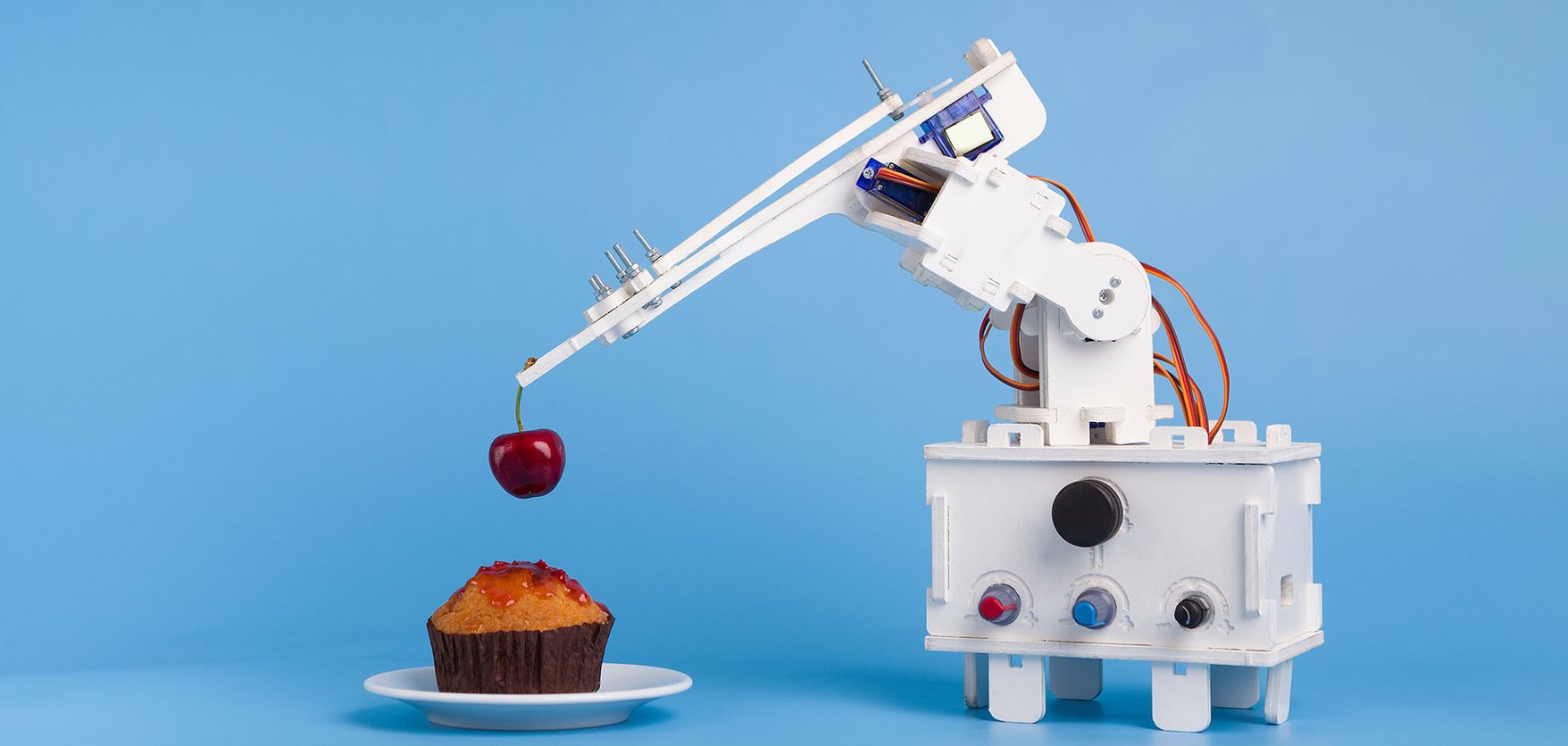 A robotic arm placing a cherry on top of a cake